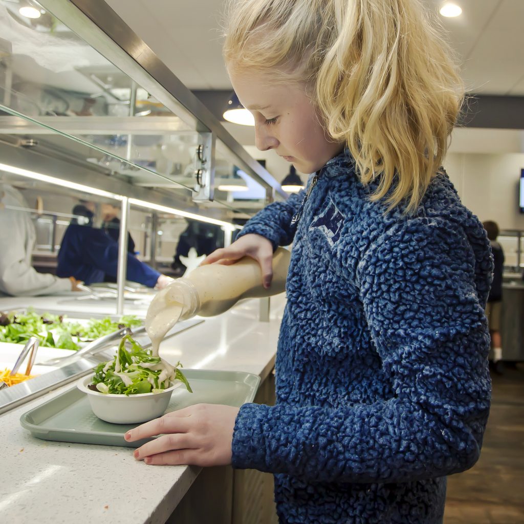 A middle school girl prepares a green salad at the salad bar of the newly-redesigned cafeteria that also features a fruit and yogurt bar.