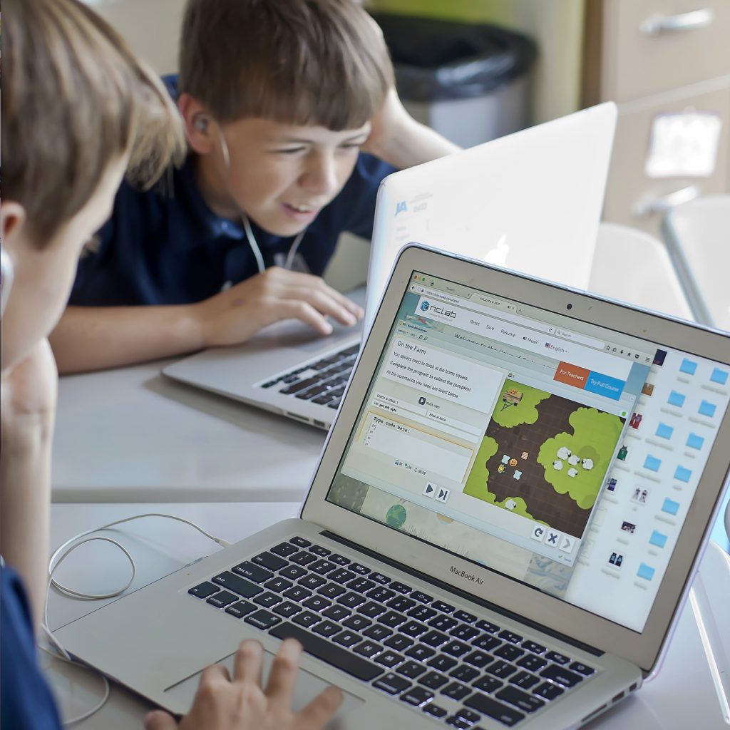 Two middle school age boys use Macbook Air computers while working on programs that teach coding, a skill valued in the workplace.